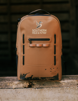 Wetland waterproof hunting backpack in Bayou Brown with the Southern Field & Flyway logo and a muddy base, on a weathered wood ledge